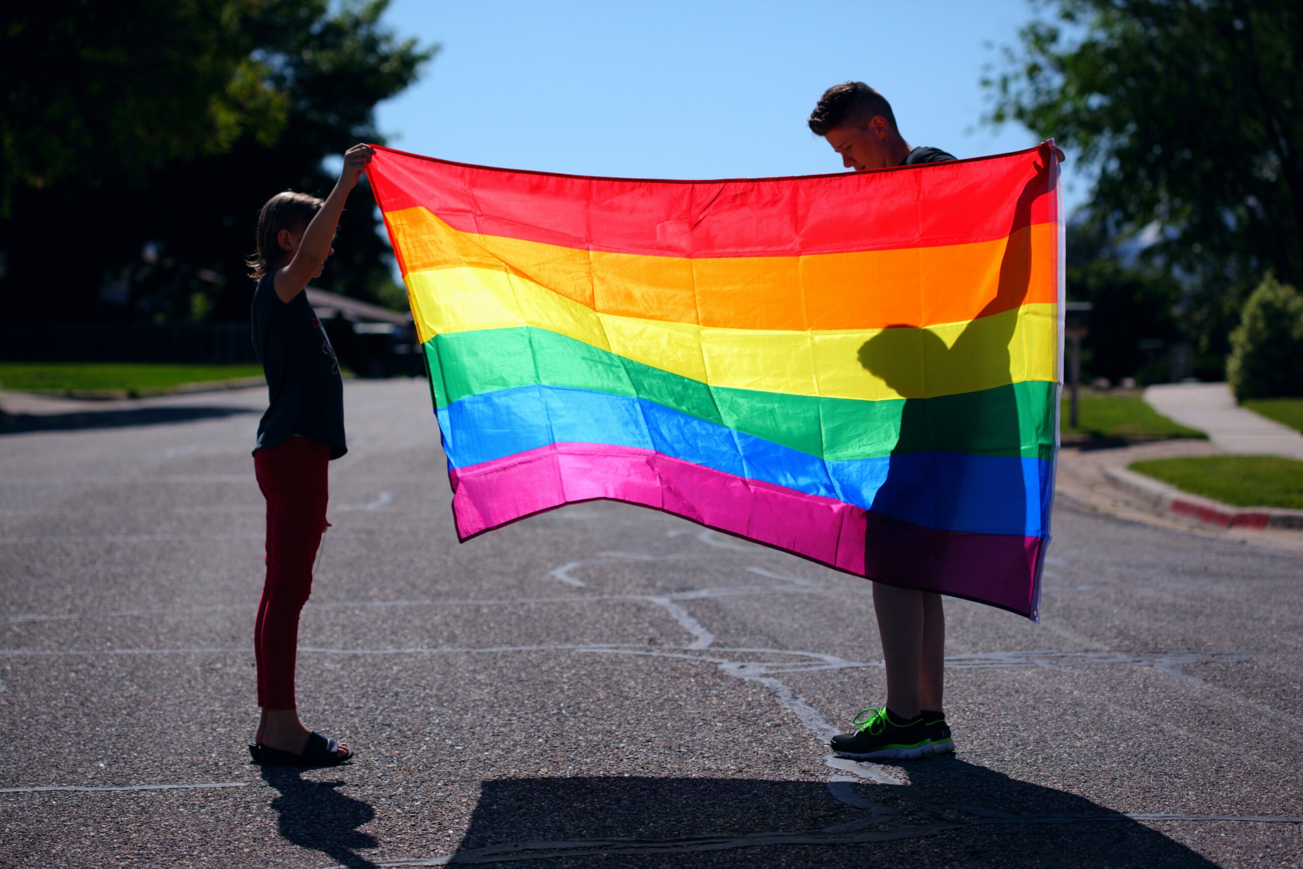 two people holding up a pride flag with the sun shining behind them